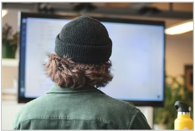 back of head man in togue looking at large screen