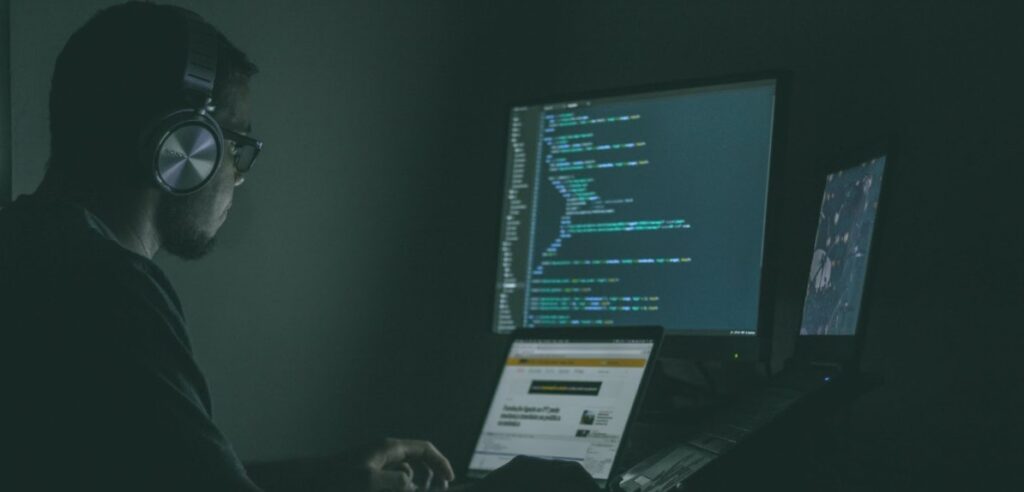 man working on computer laptops and external in dark