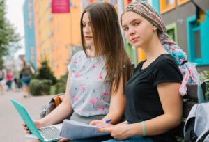 two high school girls on laptop with paper notes