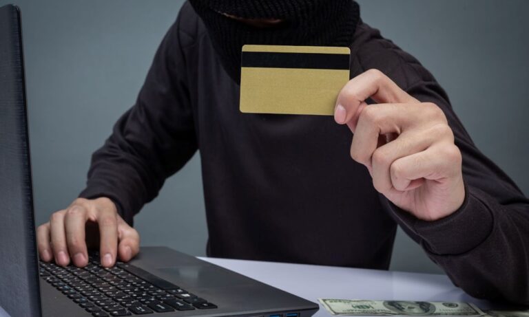 cybercrime - masked hacker with credit card in front of computer