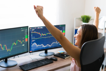 women in front of 2 computer screens showing stock charts graphs